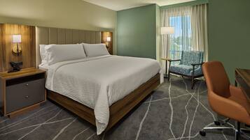 A hotel room with a large bed, a desk, a chair, and a window with curtains.