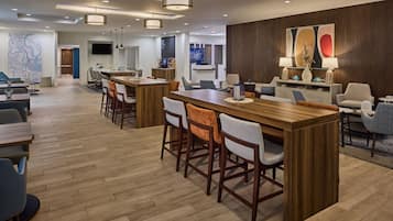A modern hotel lobby with a central bar area, seating arrangements, and a large wall-mounted TV.
