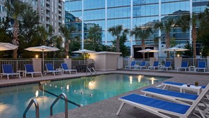 A pool area with lounge chairs and umbrellas, surrounded by palm trees and a modern building. -  Holiday Inn Express & Suites Charleston DWTN - Medical CTR by IHG (Charleston)