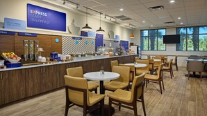 A modern breakfast area with a counter displaying various food items, seating arrangements, and a large screen advertising breakfast. -  Holiday Inn Express & Suites Charleston DWTN - Medical CTR by IHG (Charleston)