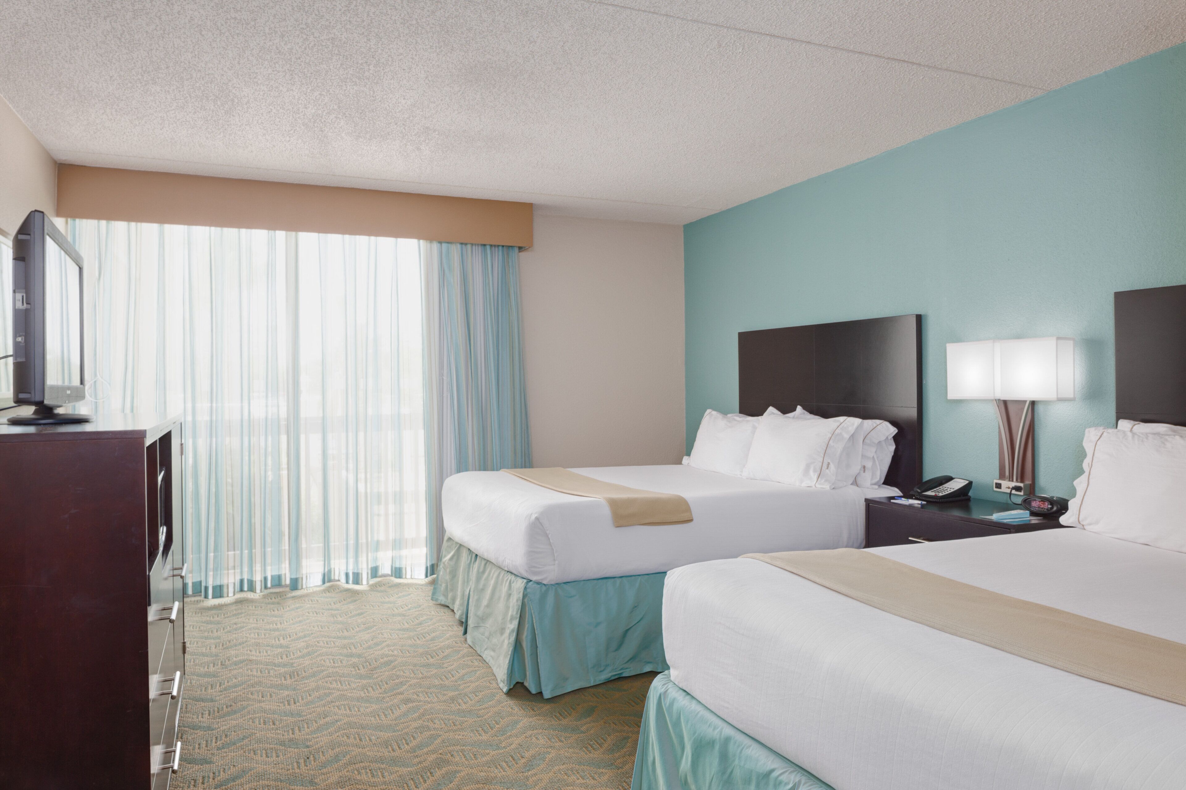 A hotel room with two beds, a desk, a telephone, and a window with curtains.