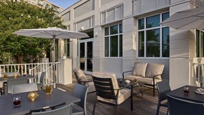 An outdoor patio with tables and chairs, umbrellas, and a view of a building with large windows. -  Holiday Inn Express & Suites Charleston DWTN - Medical CTR by IHG (Charleston)