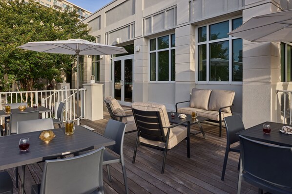 An outdoor patio with tables and chairs, umbrellas, and a view of a building with large windows. -  Holiday Inn Express & Suites Charleston DWTN - Medical CTR by IHG (Charleston)