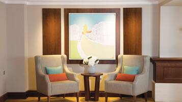 A room with two armchairs, a small table with a vase of flowers, and a large painting on the wall.