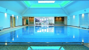 A large indoor swimming pool with a skylight ceiling, clear glass doors leading outside, and a tiled floor.
