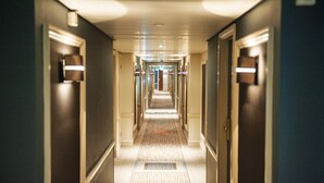 A hotel hallway with a carpeted floor, doors on both sides, and overhead lighting.