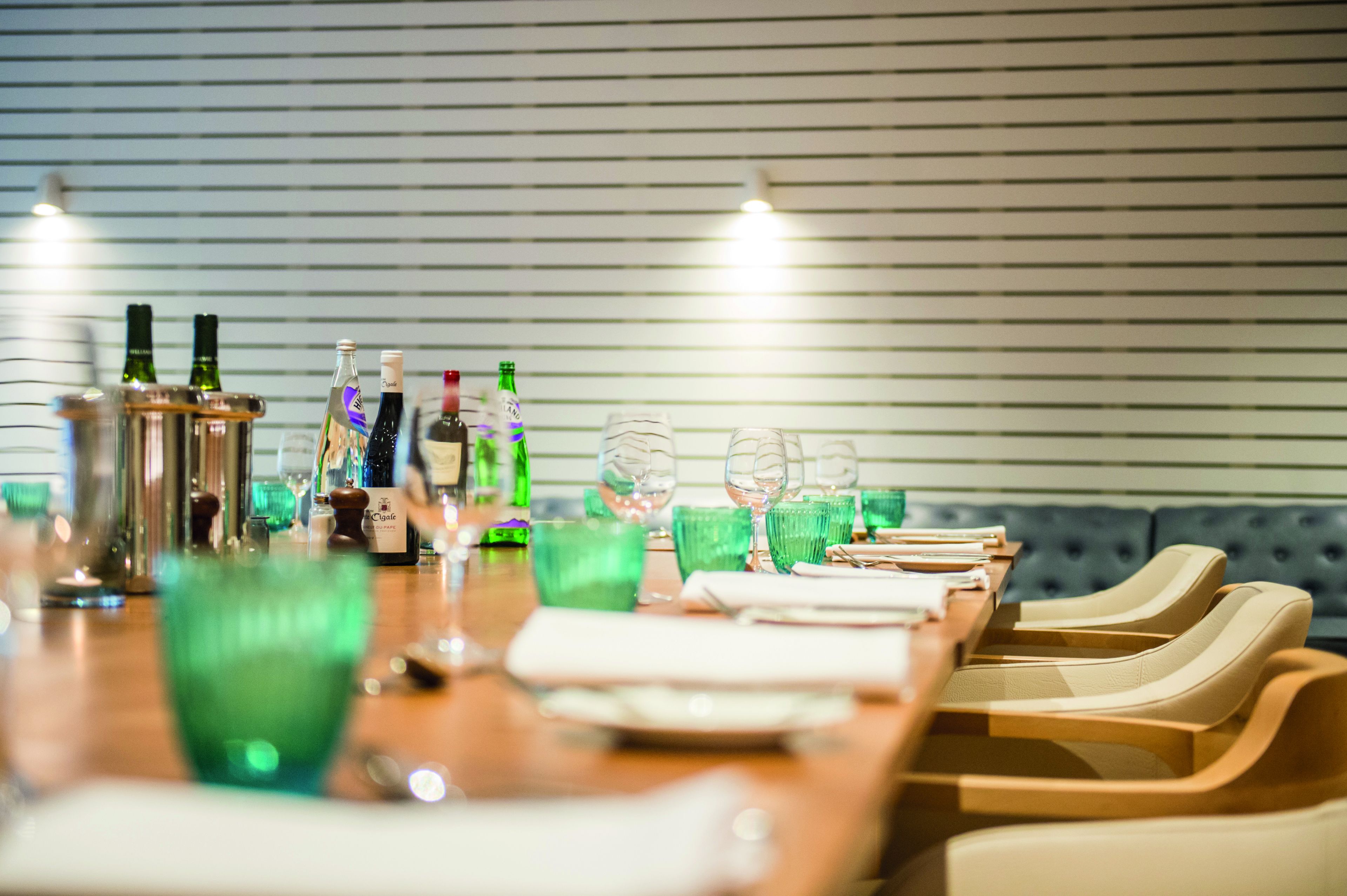 A dining table set with green glasses, plates, and bottles, with a blue upholstered sofa in the background.