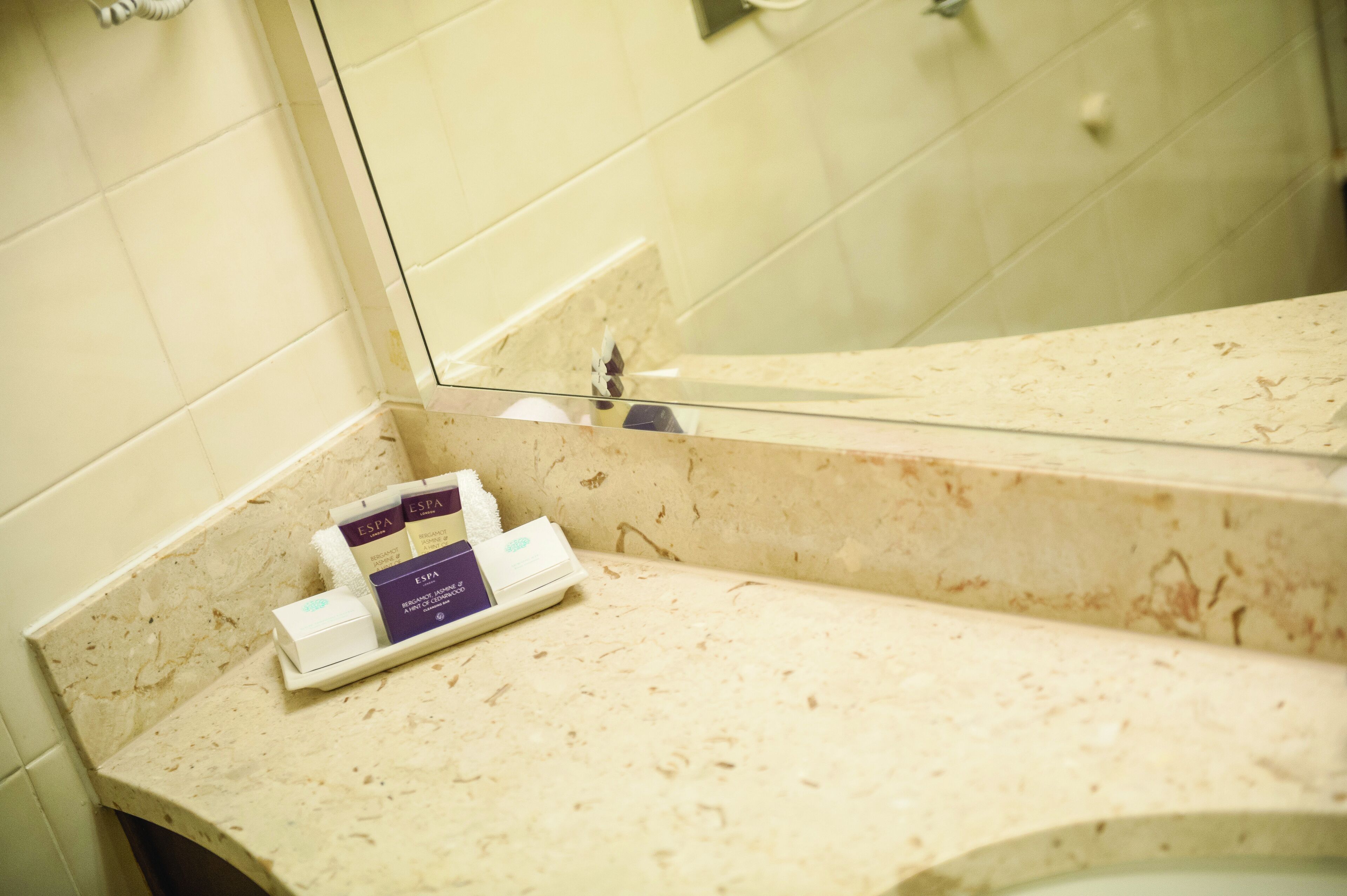 A bathroom with a beige marble countertop, a glass shower enclosure, and a mirror reflecting the shower area.