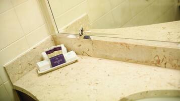 A bathroom with a beige marble countertop, a glass shower enclosure, and a mirror reflecting the shower area.