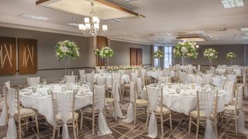A banquet hall with round tables, white tablecloths, and floral centerpieces.