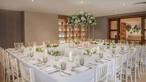A long dining table set for a formal event with white tablecloths, candles, and floral centerpieces.