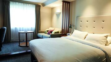 A hotel room with a large bed, a sofa, a chair, and a small table.