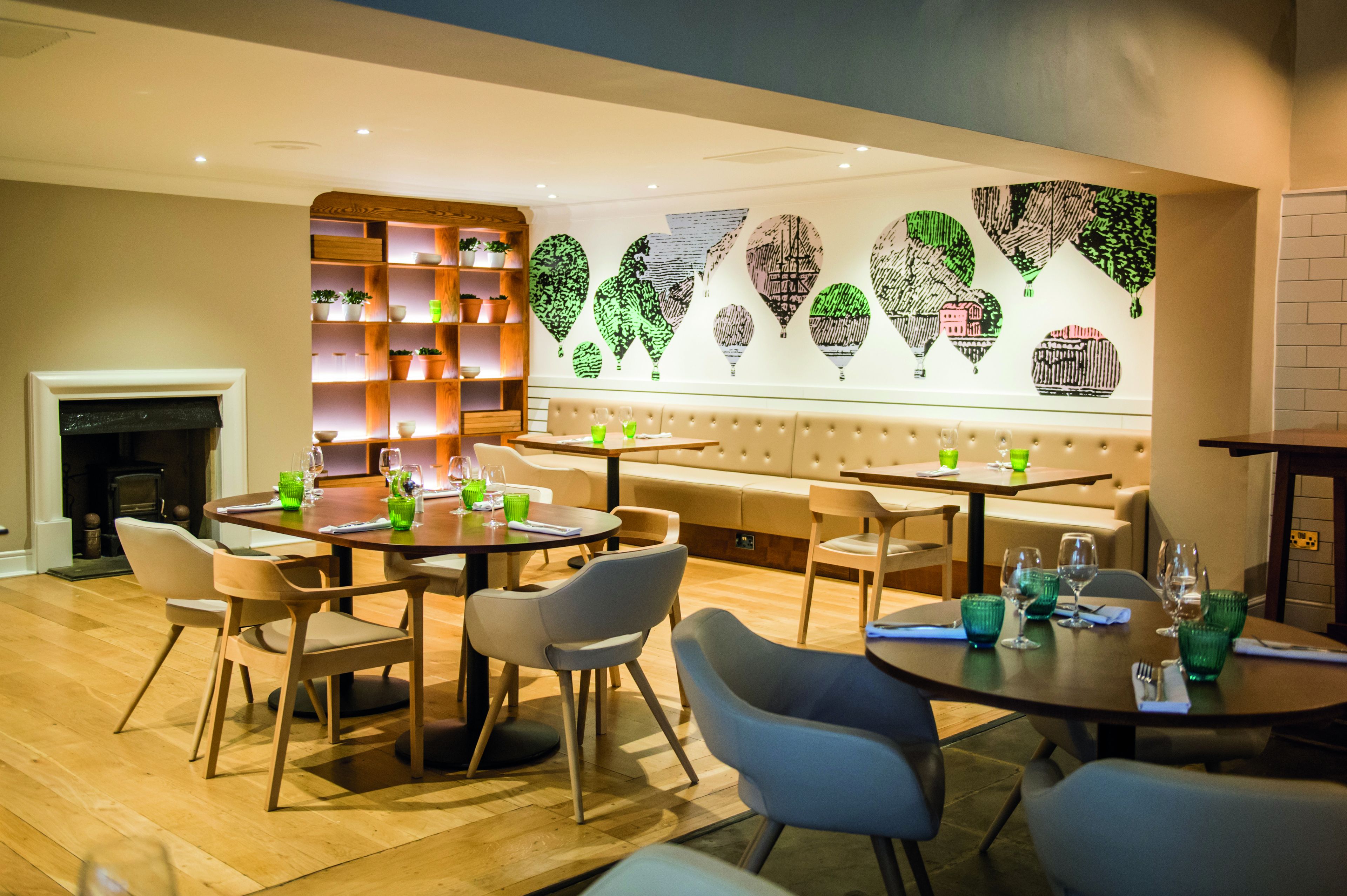 A modern restaurant with round tables, cushioned seating, and a decorative wall with abstract art.