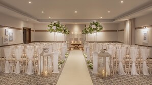 A hotel chapel with white chairs, a white aisle, and floral decorations.