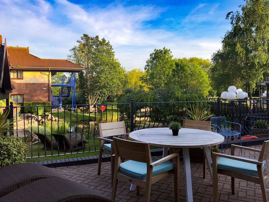 An outdoor patio with a round table and chairs, surrounded by a metal fence.