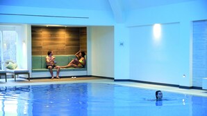 A swimming pool with two people sitting on a bench, a wooden wall, and a tiled wall.