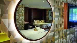 A bedroom with a large mirror, two beds, a nightstand, and a TV.