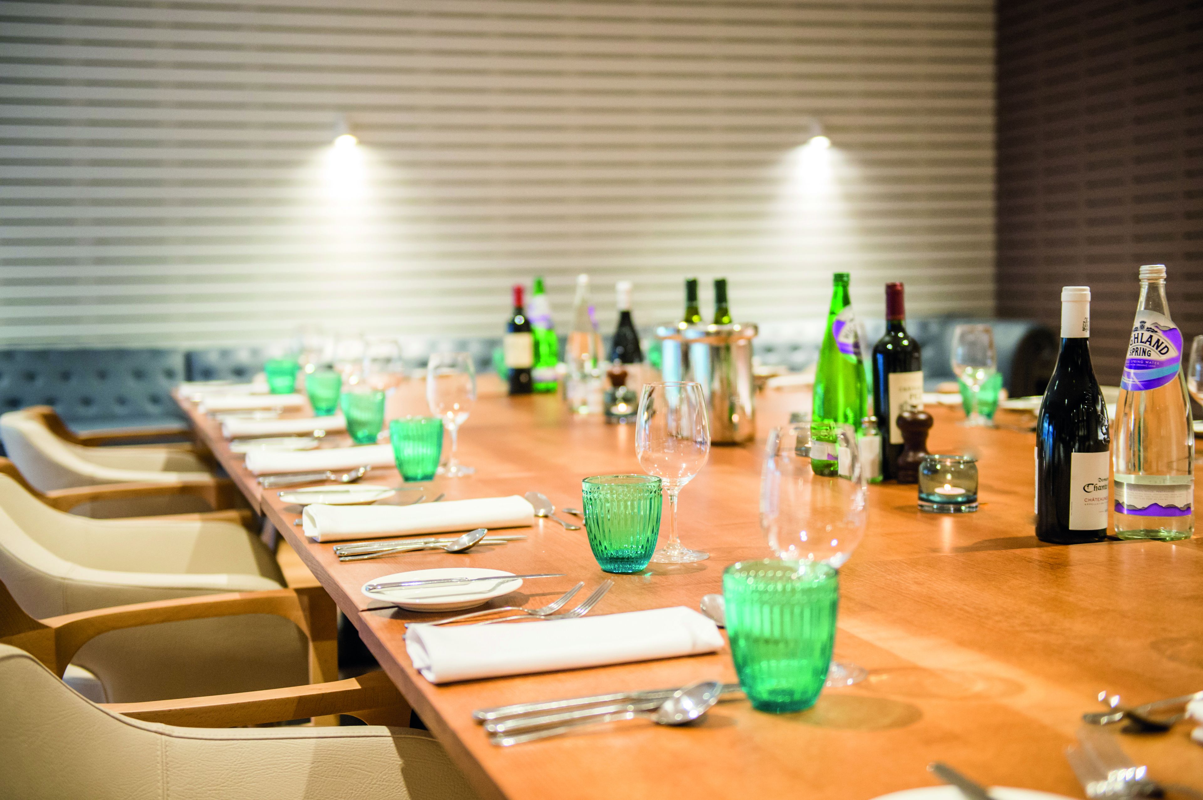 A long dining table set with green glassware, plates, and silverware, with bottles of wine and glasses on the table.