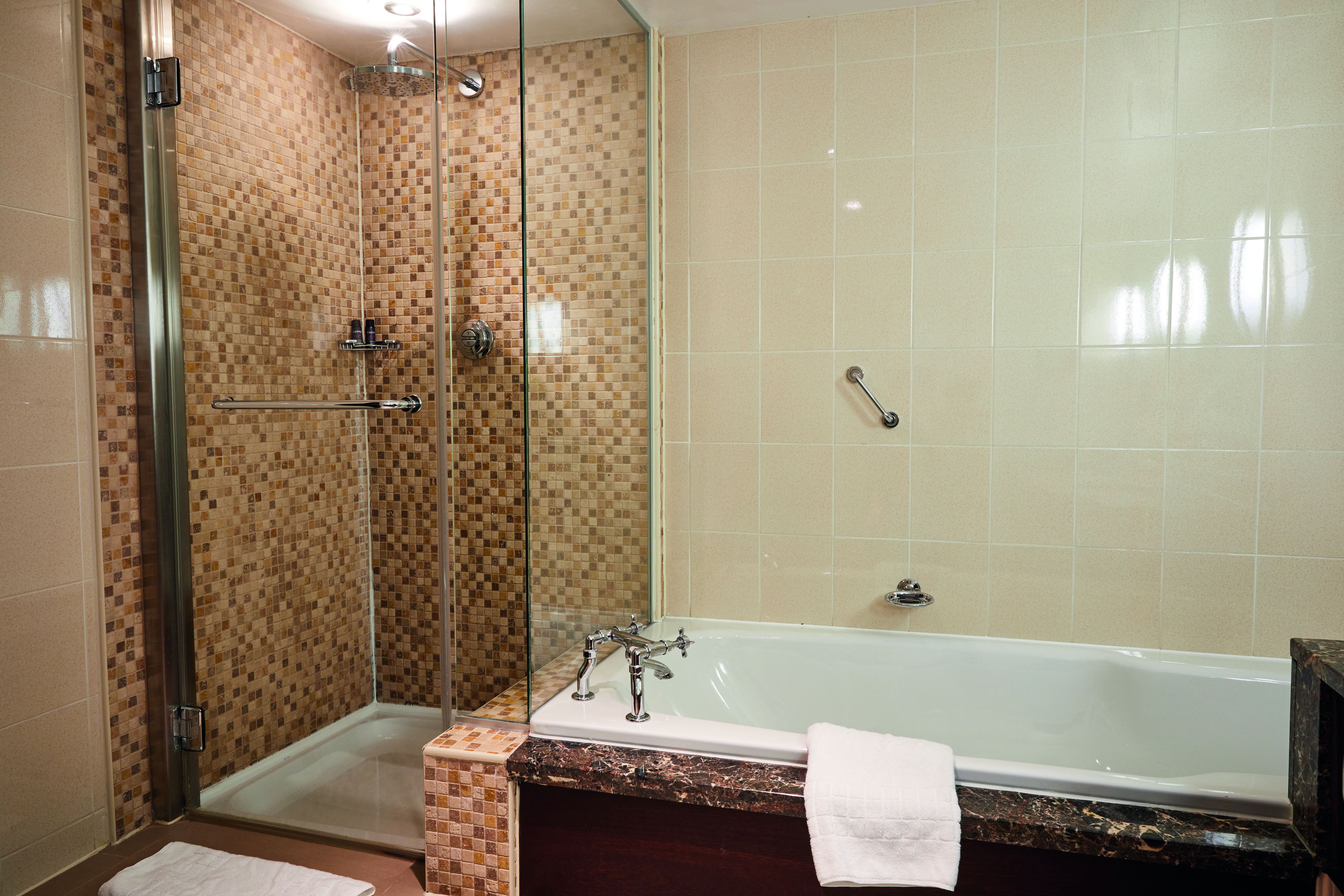 A bathroom with a glass-enclosed shower, a bathtub, and a tiled wall.