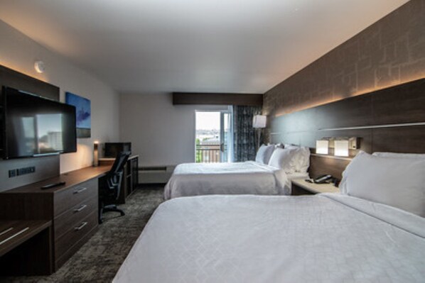 A hotel room with two beds, a desk, a television, and a balcony with a view.