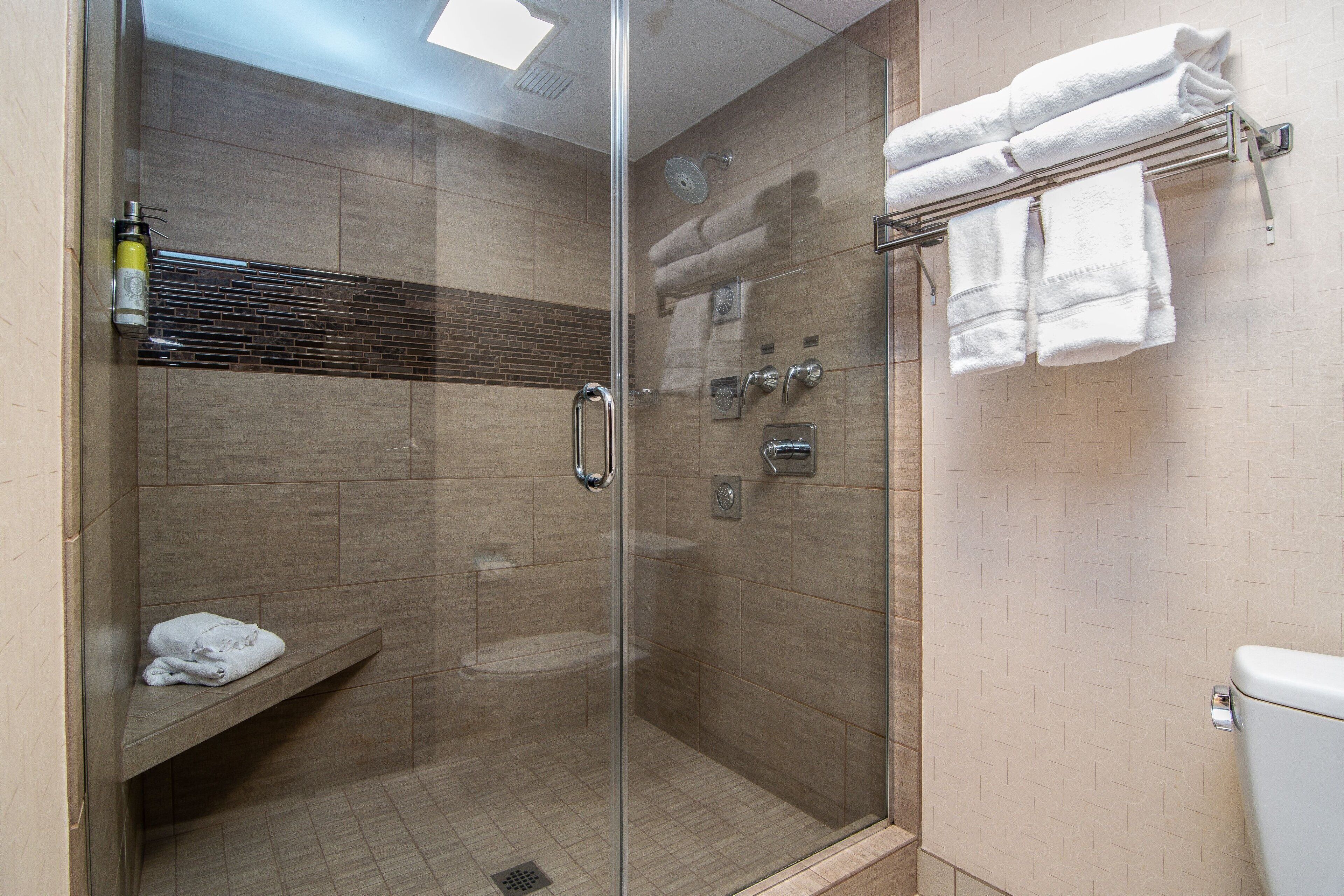 A glass-enclosed shower with a bench, a towel rack, and a toilet.