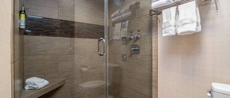 A glass-enclosed shower with a bench, a towel rack, and a toilet.