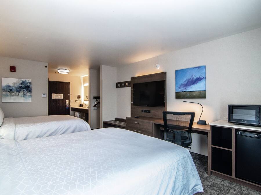 Habitación de hotel con dos camas, un escritorio con computadora, un televisor y un microondas.