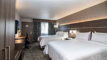 A hotel room with two beds, a desk with a chair, a wardrobe, and a mirror.