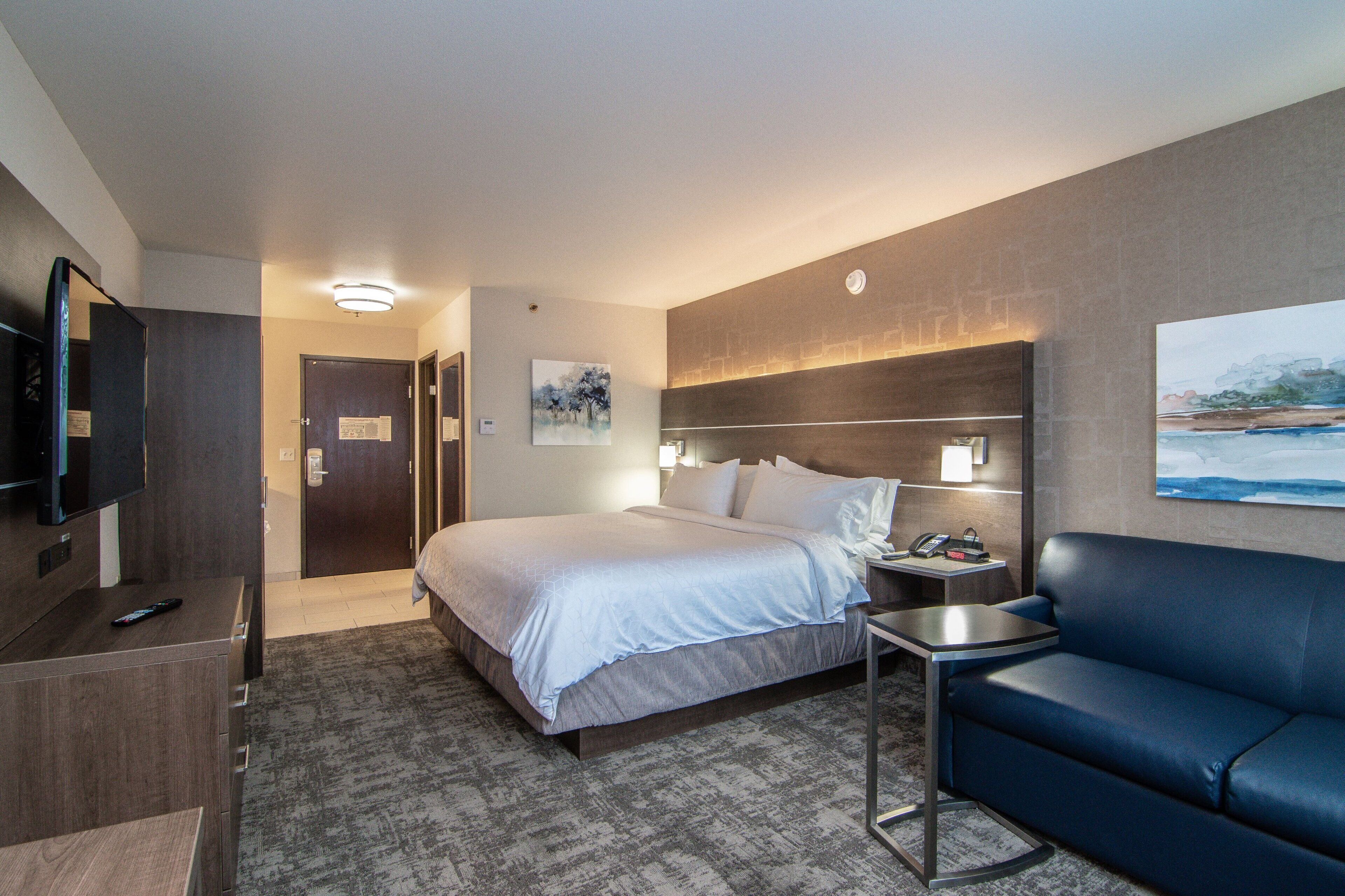 A hotel room with a bed, a TV, a desk, a chair, and a painting on the wall.