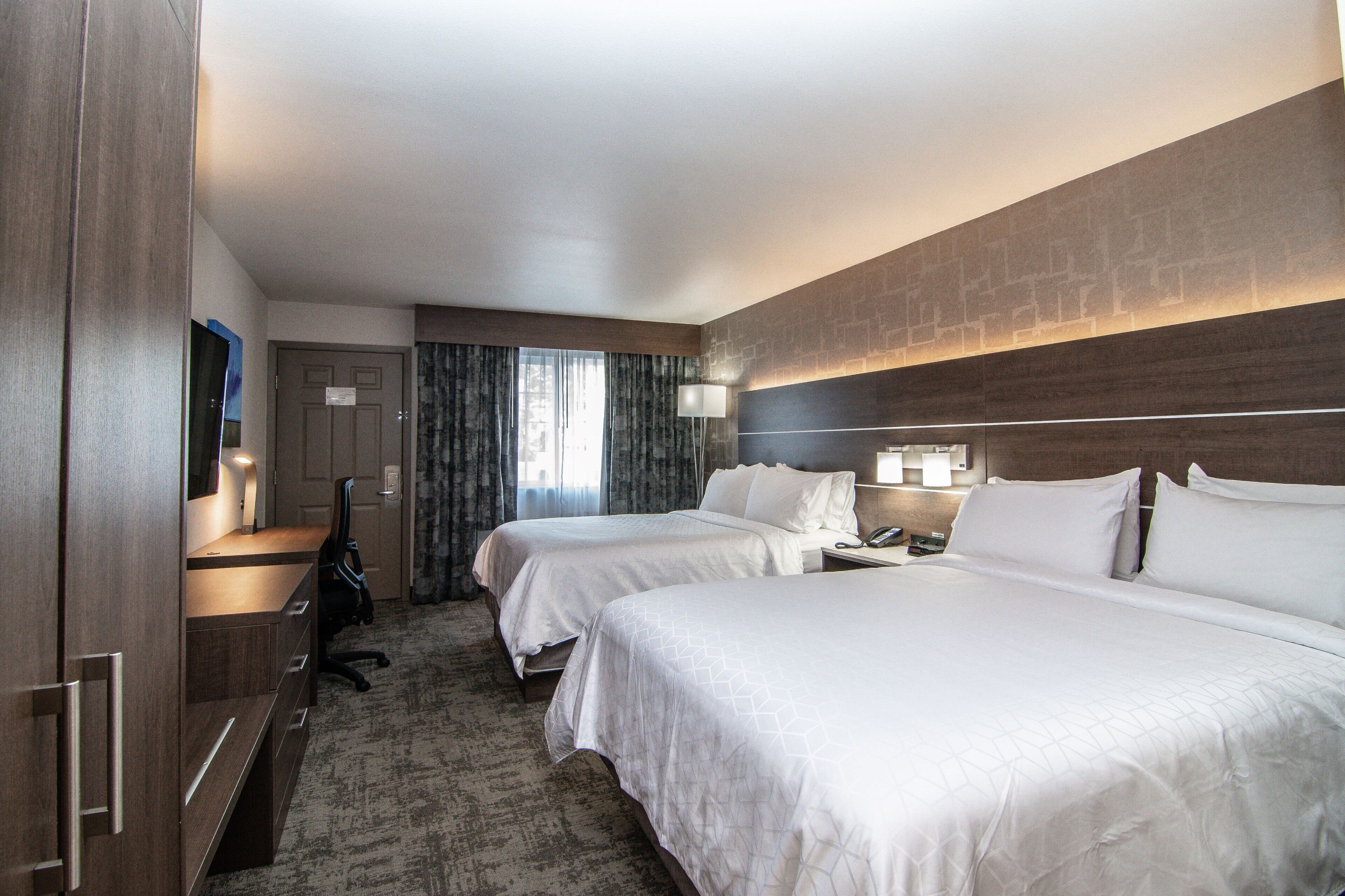 A hotel room with two beds, a desk with a chair, a wardrobe, and a bathroom door.
