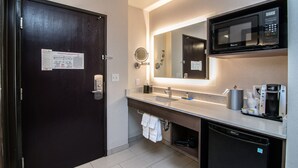 A modern hotel bathroom with a dark wooden door, a sink with a mirror, a microwave, and a coffee maker. - Holiday Inn Express Spokane Downtown by IHG (Spokane)