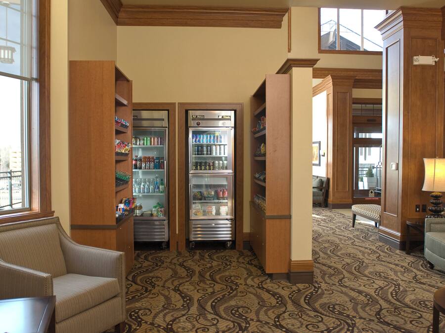 A hotel lobby with a patterned carpet, a seating area with a chair, and two beverage dispensers.