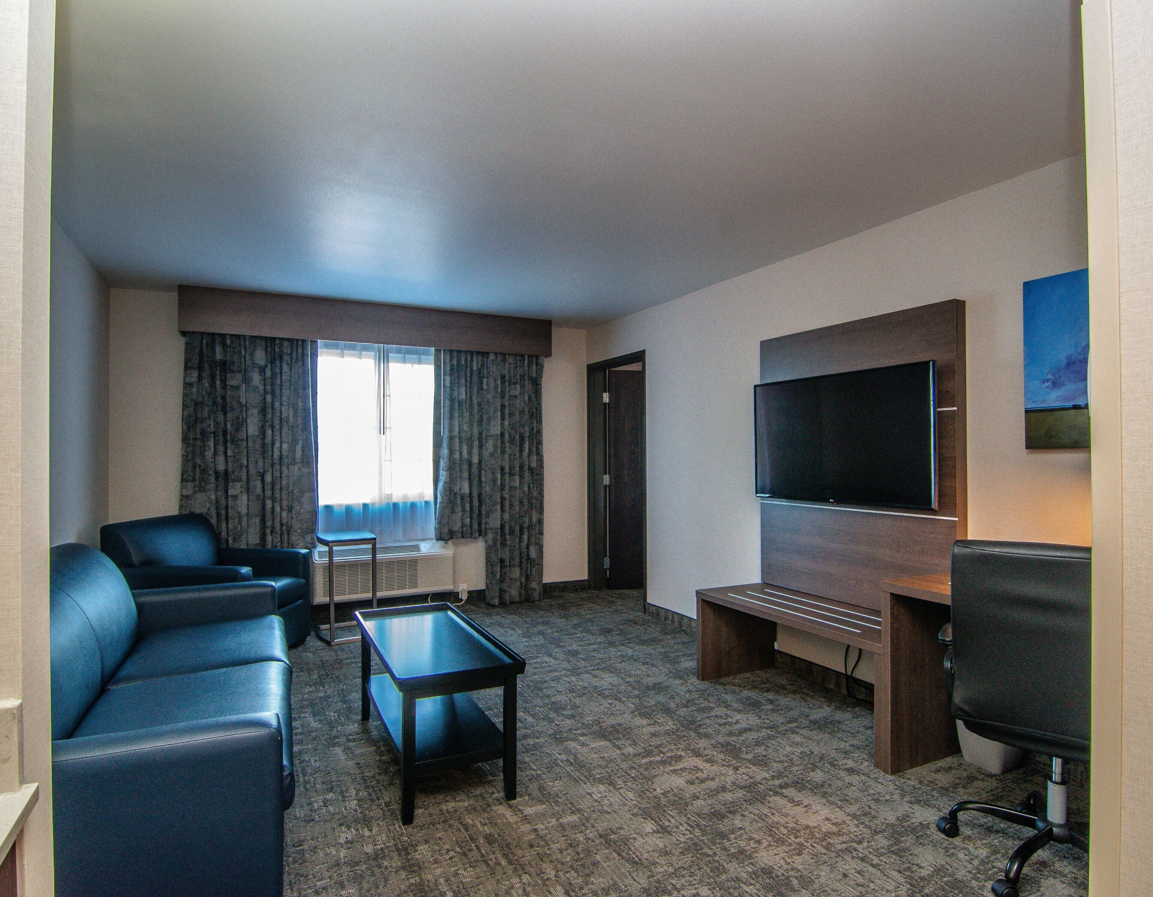 A hotel room with a sofa, a coffee table, a flat-screen TV, and a carpeted floor.