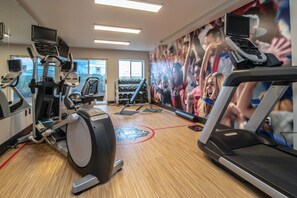 A gym with various exercise equipment, including treadmills and stationary bikes, and a large motivational mural on the wall.