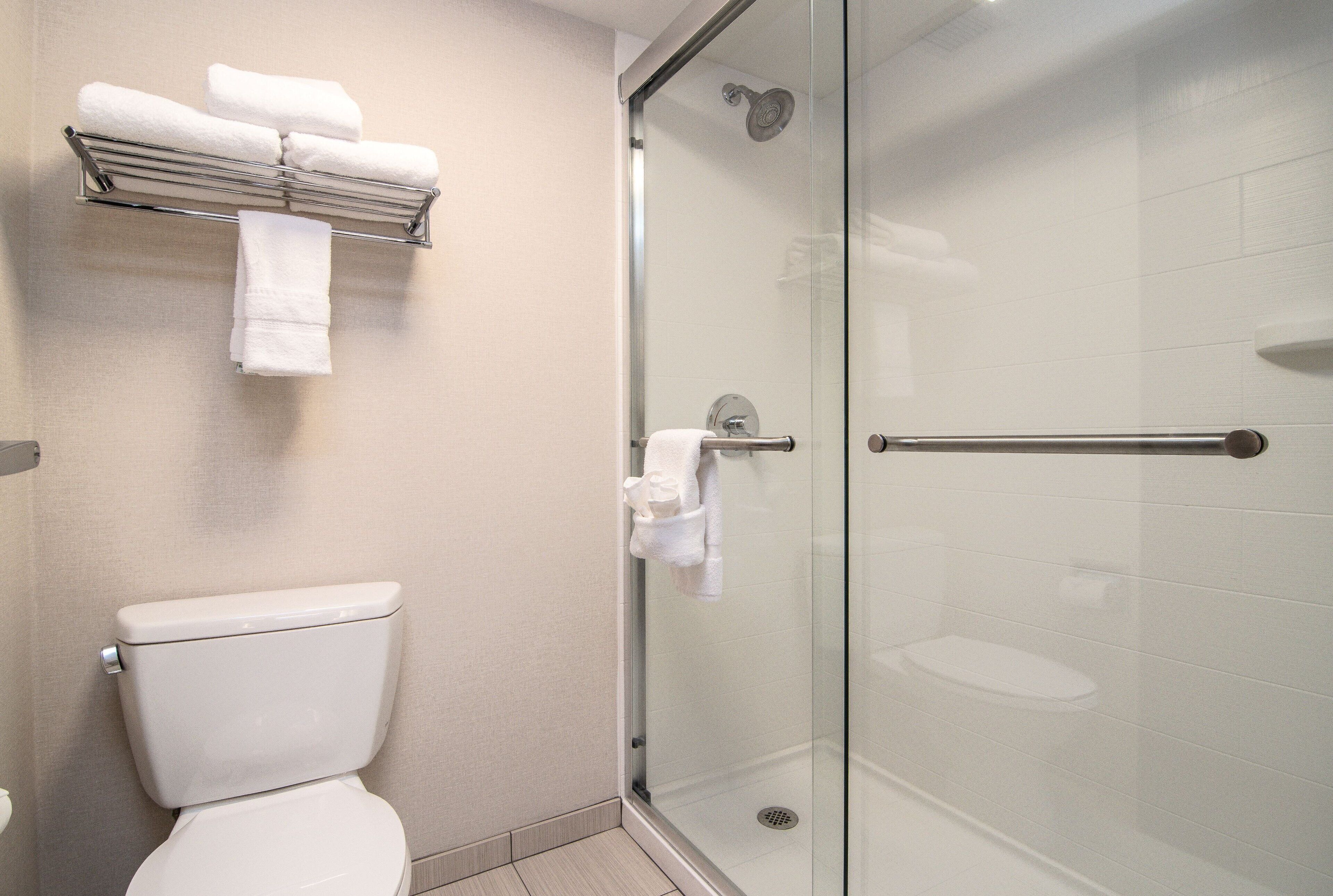 Ein modernes Badezimmer mit einer gläsernen Duschkabine, einer weißen Toilette und einem Handtuchhalter mit ordentlich gefalteten Handtüchern.