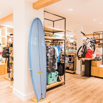 A retail store with wooden flooring, clothing racks, and a surfboard display.