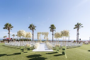 An outdoor wedding ceremony with a white aisle, white chairs, and floral decorations.