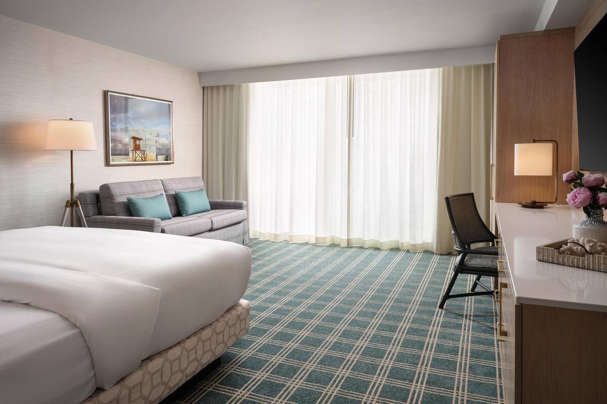 Une chambre d’hôtel avec un lit, un canapé, un bureau, une chaise, une lampe et un tableau au mur.