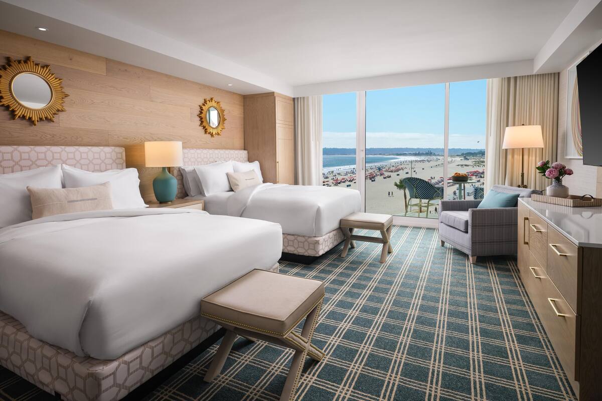 Une chambre d’hôtel avec un grand lit, un lit plus petit, un bureau, une chaise et une vue sur la plage.
