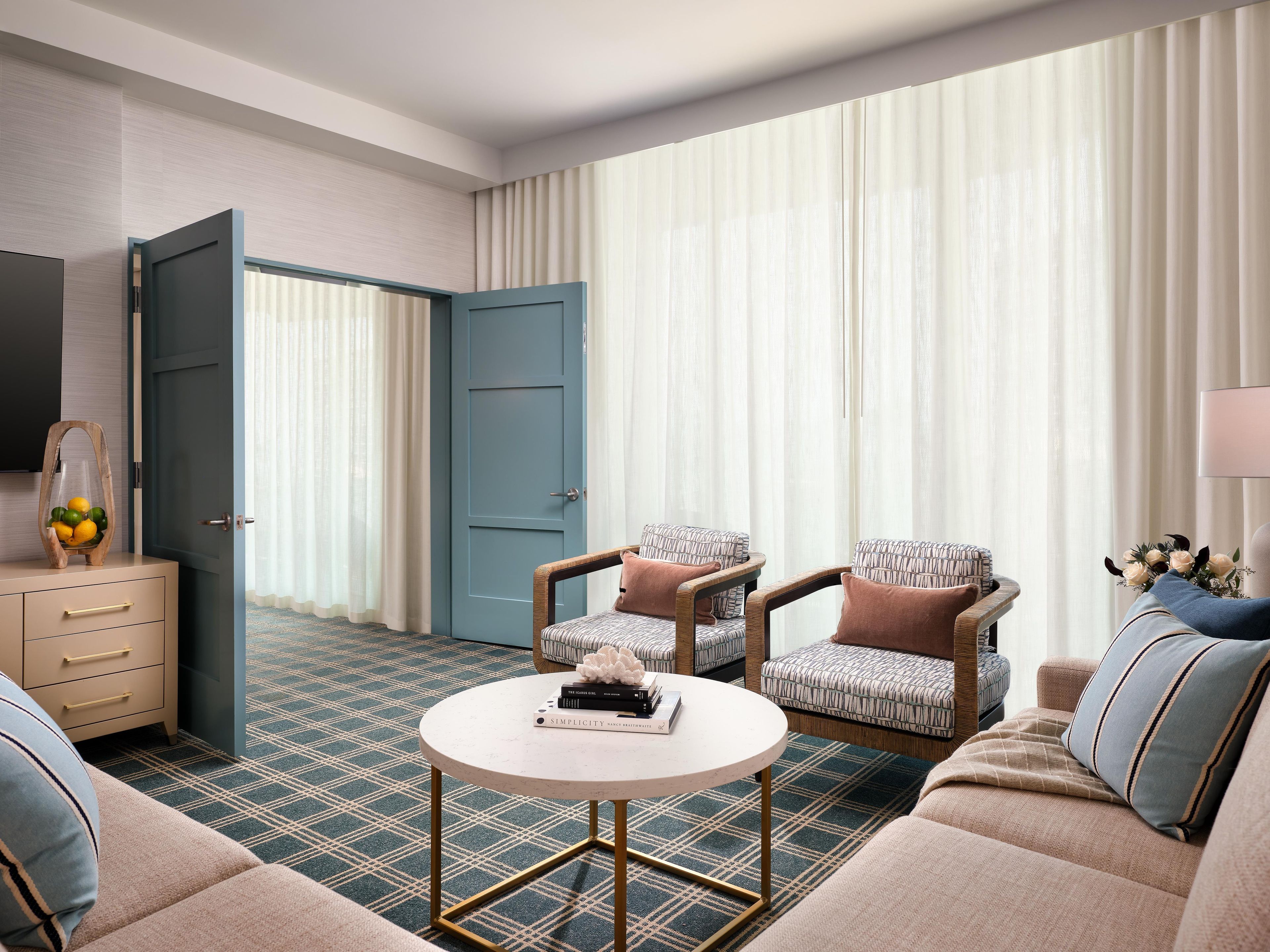 Une chambre d’hôtel comprenant un canapé, deux fauteuils, une table basse, un téléviseur et une porte donnant sur une autre pièce.