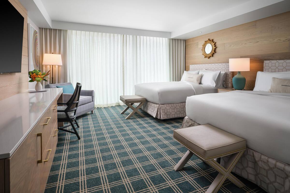 Une chambre d’hôtel avec un lit, un bureau, une chaise, une télévision et une fenêtre avec des rideaux.
