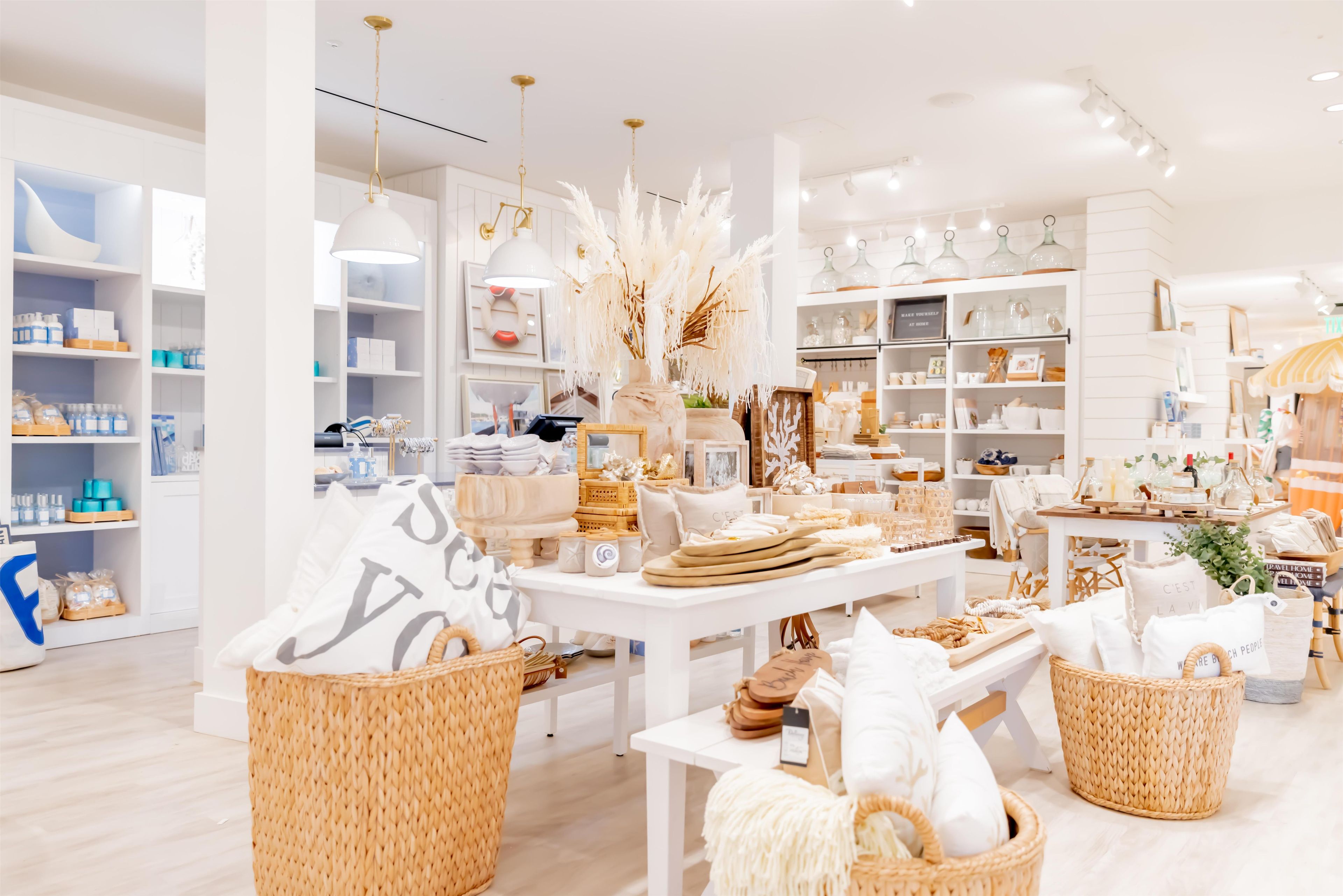 A well-lit, spacious boutique hotel interior with white walls, wooden flooring, and a variety of neatly arranged home decor items on shelves and tables.