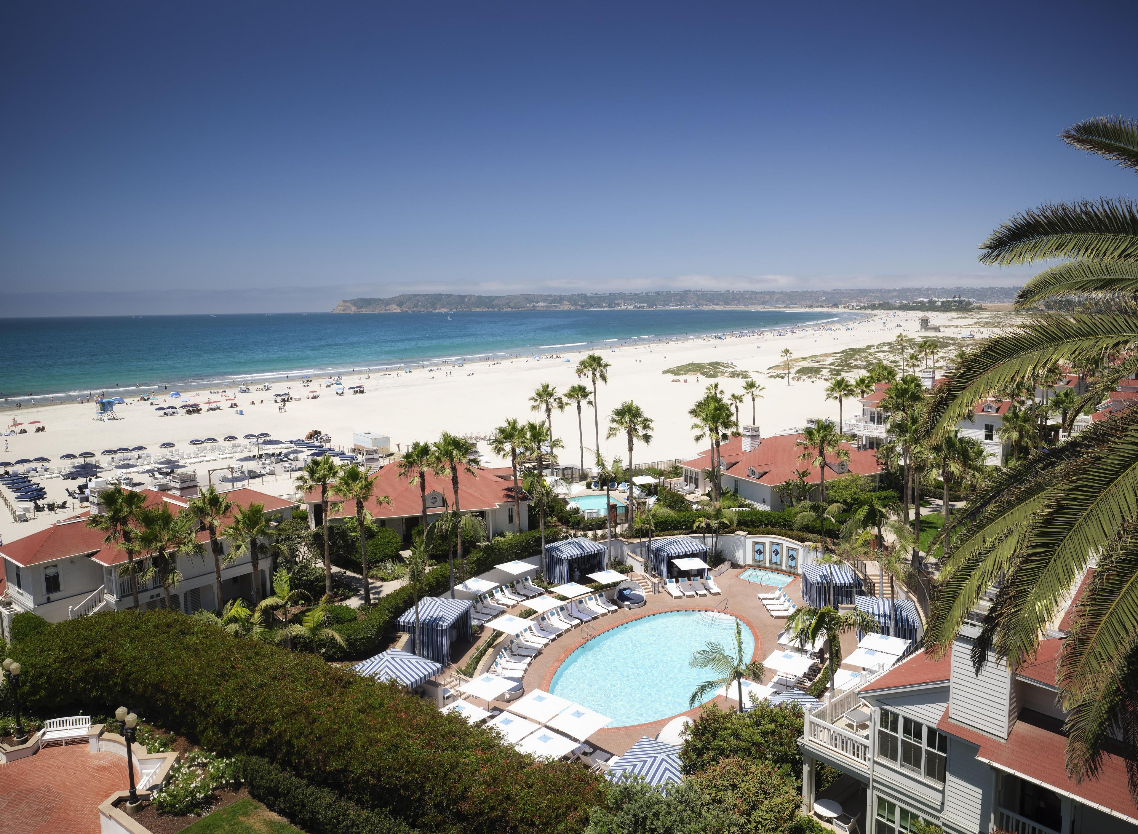 A resort with a swimming pool, beach, and palm trees.