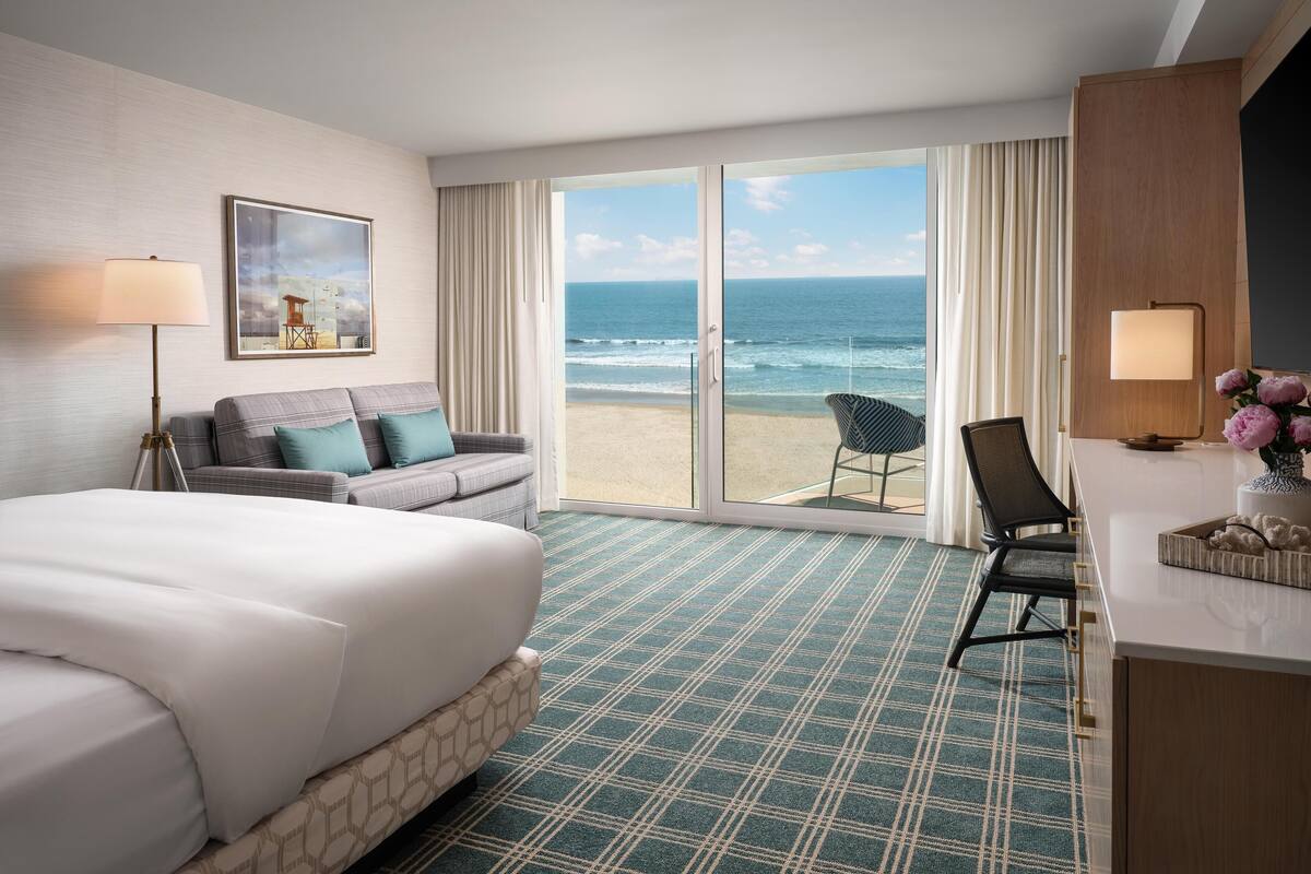 Une chambre d’hôtel avec un lit, un canapé, une chaise, un bureau et une vue sur la plage.
