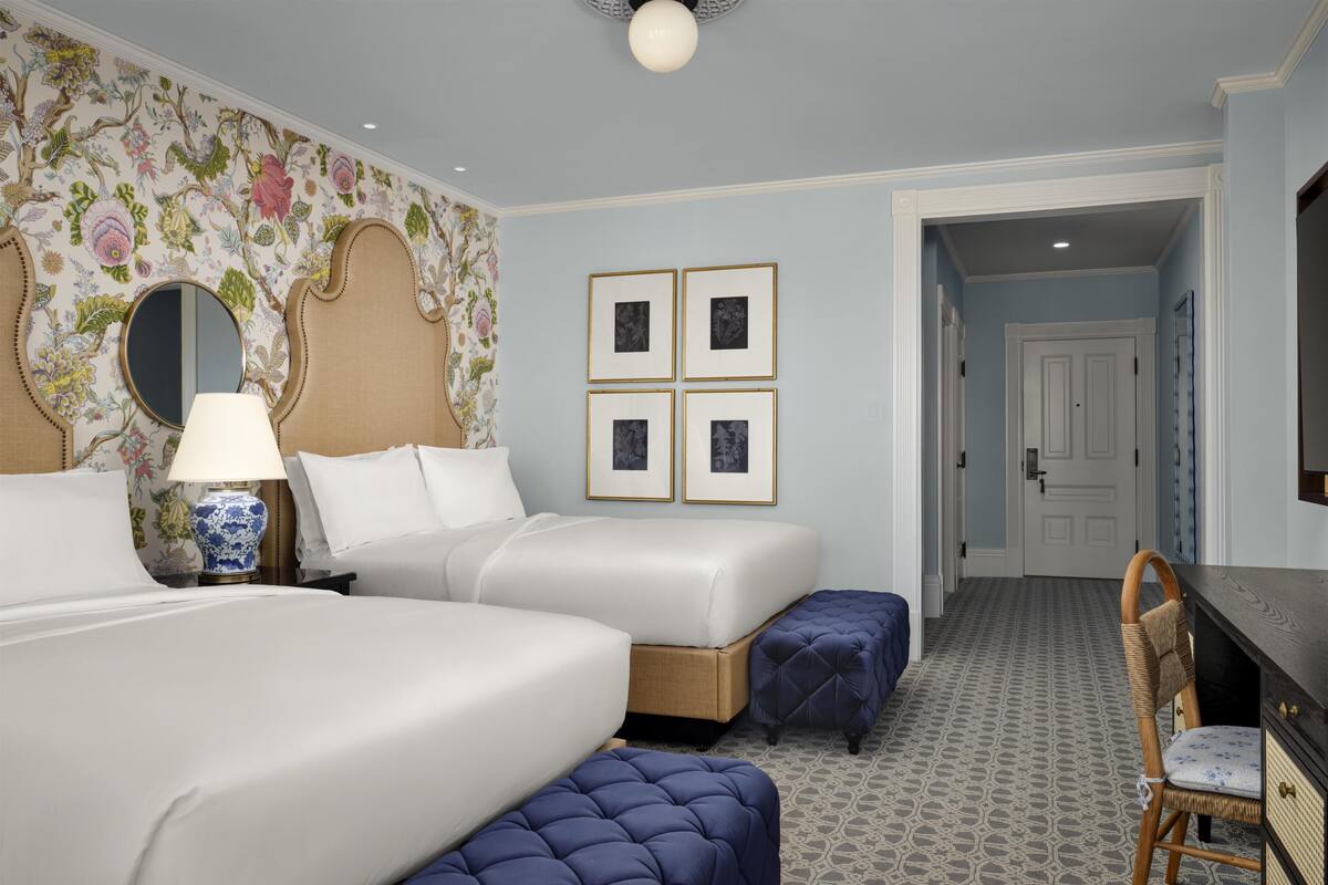 Une chambre d’hôtel avec deux lits, un bureau, une chaise, une lampe et un miroir.
