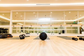 A gym with exercise equipment, large windows, and a wooden floor.