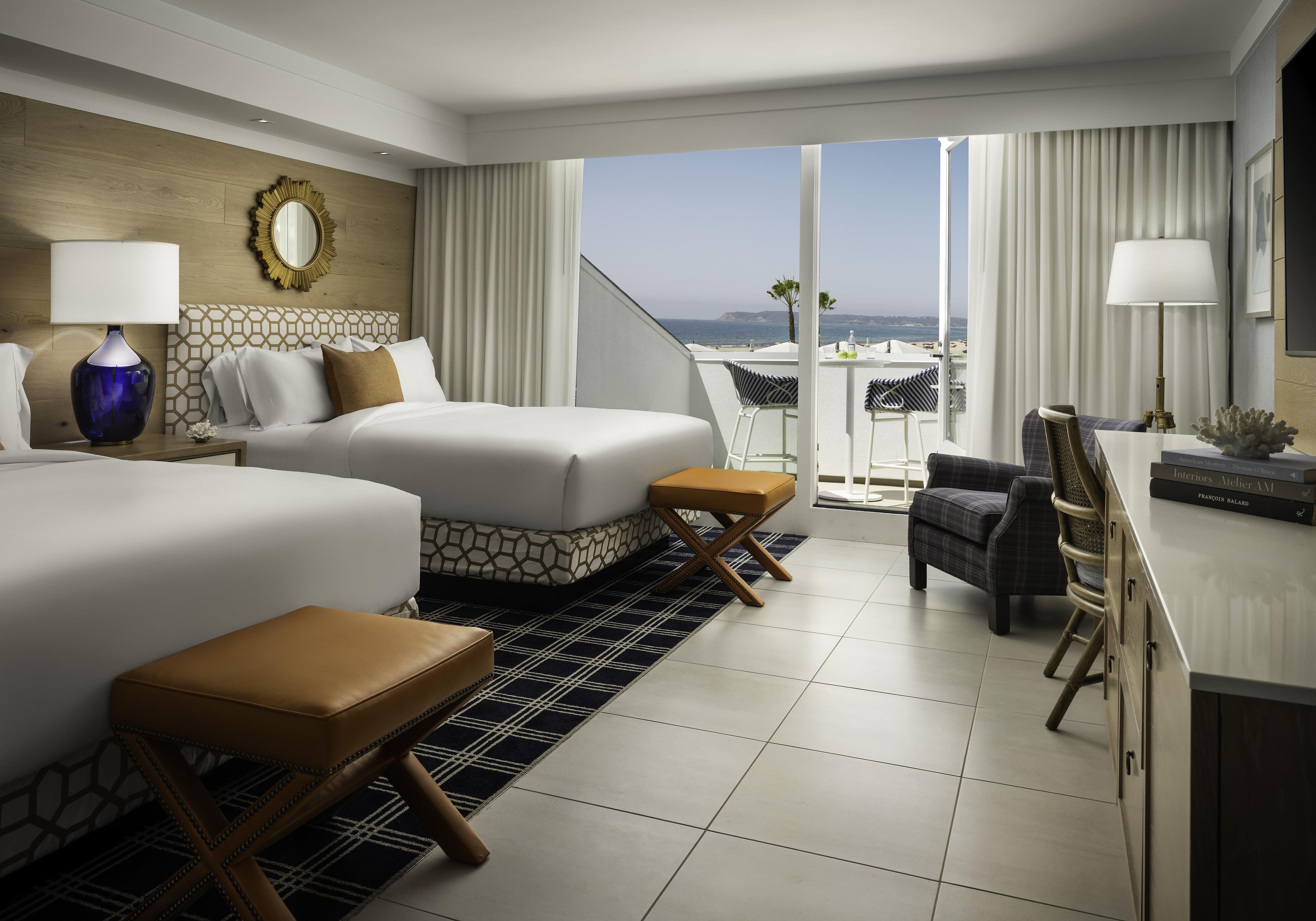 Una habitación de hotel con una cama grande, una cama más pequeña, un escritorio con silla y vista al océano.