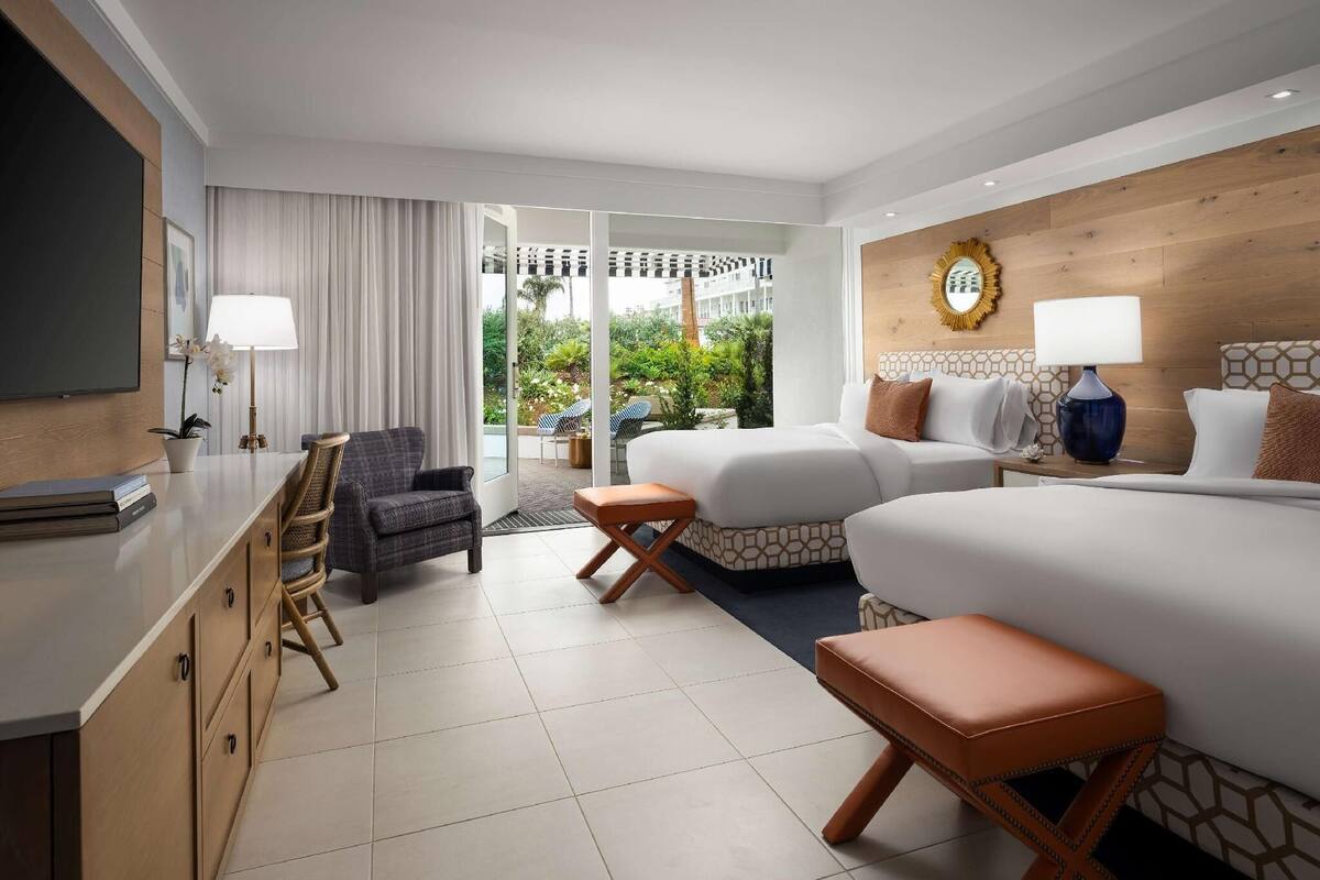 A hotel room with a bed, two bedside tables, a desk, a chair, and a view of the outdoor garden.