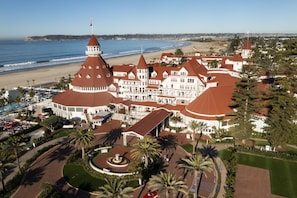 Un hotel grande de varios pisos con un patio central, rodeado por una playa y vistas al océano.