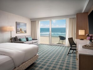 A hotel room with a bed, a sofa, a chair, a desk, and a view of the beach.